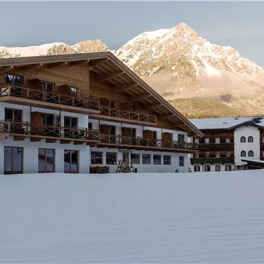 A beautiful alpine landscape with snow-covered mountains. In the foreground are modern, rustic buildings.