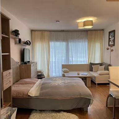 A bright and cozy room with a double bed and a seating area. Large windows provide plenty of daylight.