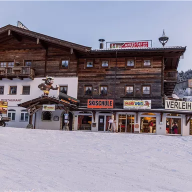 A traditional wooden building in the snow with signs for ski school and rental service. The surroundings are wintry and inviting for winter sports enthusiasts.