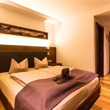 A cozy bedroom with a large bed and wooden floor. The warm colors and soft lighting create an inviting atmosphere.
