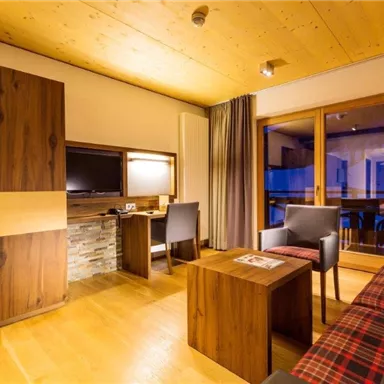 A modern room with wood paneling and a cozy atmosphere. It features a television, a desk, and access to a balcony.