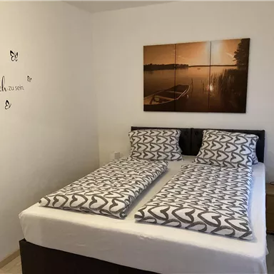 Ein gemütliches Schlafzimmer mit einem Doppelbett und modernen Bettwäsche. An der Wand hängt ein schönes Bild eines Bootes am See.