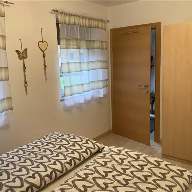 Ein gemütliches Schlafzimmer mit zwei Betten und einem Schrank. Die Wände sind mit Vorhängen und dekorativen Elementen geschmückt.