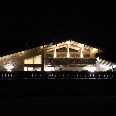 A modern house at night, beautifully illuminated. The design combines wood and stone, creating a warm atmosphere.