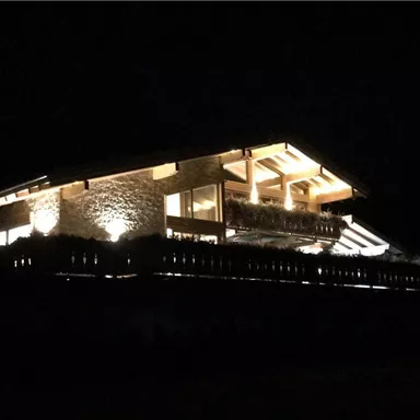 A modern wooden house illuminated at night. The light-filled balcony and warm lights create a cozy atmosphere.
