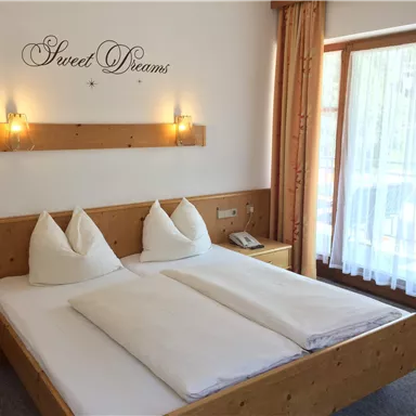 A cozy bedroom with a double bed and two pillows. The room has large windows and a warm wooden paneling.