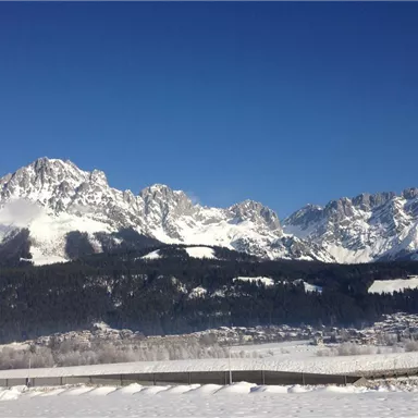 An impressive mountain landscape with snow-covered peaks and a clear blue sky. The surroundings are tranquil and picturesque, ideal for winter sports activities.
