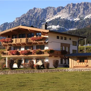 A beautiful house in nature with colorful flowers on the balcony. Majestic mountains rise in the background.