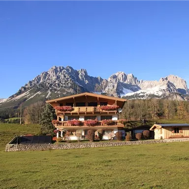 A beautiful house with a wooden veranda in a picturesque mountain landscape. Impressive mountains and a blue sky can be seen in the background.