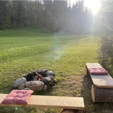 Ein gemütlicher Lagerfeuerplatz mit Holzbank und Kissen.