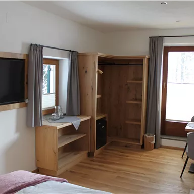 A cozy room with wooden details, a television, and a table. The room has large windows that let in plenty of light.