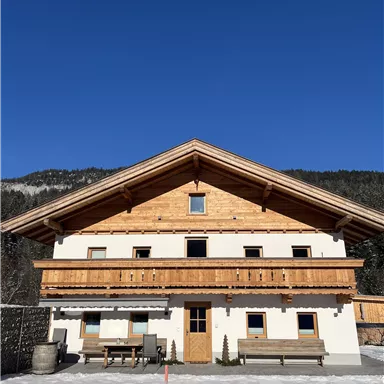 A typical Alpine house with wooden cladding and a balcony. The clear blue sky and the snow-covered surroundings enhance the idyllic atmosphere.
