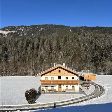A cozy house nestled in a snowy landscape. In the background, green mountains stretch out under a clear blue sky.