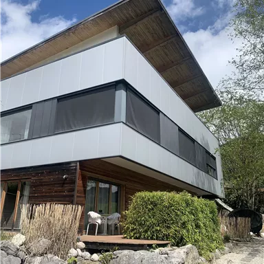 Ein modernes Wohnhaus mit einer Kombination aus Holz- und Metallfassade. Umgeben von grüner Vegetation und Steinuntergrund.