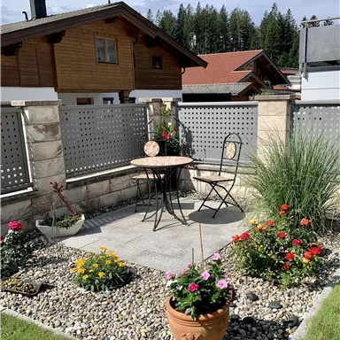 Ein schöner Gartenbereich mit einem Tisch und einem Stuhl. Bunte Blumen und ein gepflasterter Boden schaffen eine einladende Atmosphäre.