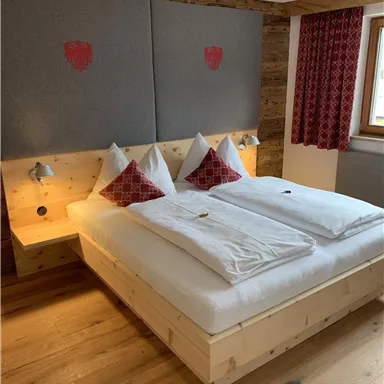Ein gemütliches Schlafzimmer mit einem großen Bett, rotem Dekor und Holzfußboden. Die Wände sind in neutralen Farben gehalten und sorgen für eine einladende Atmosphäre.