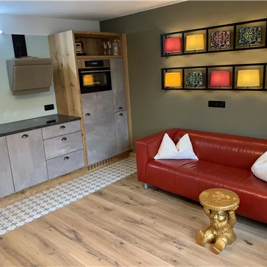 Eine moderne Küche mit Holz- und Metalldetails. Ein rotes Sofa mit weißen Kissen und ein goldener Beistelltisch vervollständigen den Raum.
