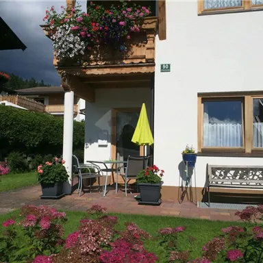 A charming house with blooming flowers in the garden. A yellow umbrella stands next to a table and chairs outdoors.