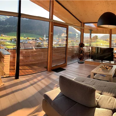 Ein modernes Wohnzimmer mit großen Fenstern und Blick auf die Berge. Die Möbel sind komfortabel und stilvoll eingerichtet.