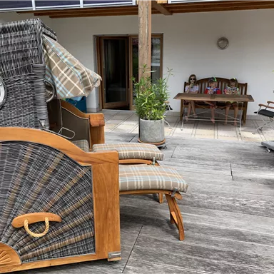 Eine gemütliche Terrasse mit einem Sonnenstuhl und einem Esstisch im Hintergrund. Pflanzen in Töpfen verleihen dem Raum eine einladende Atmosphäre.