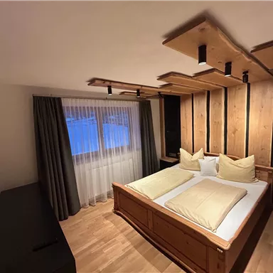 A stylish bedroom with two beds and wooden details. Large windows let in natural light.