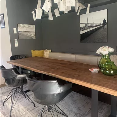 Ein moderner Essbereich mit einem großen Holztisch und schwarzen Stühlen. An der Wand hängen Bilder und Notizen, die eine gemütliche Atmosphäre schaffen.
