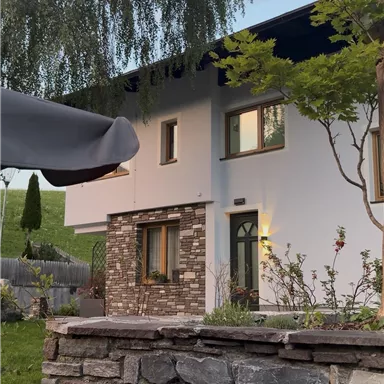 A modern house with a beautiful garden and a stone wall. The surroundings are green and inviting.