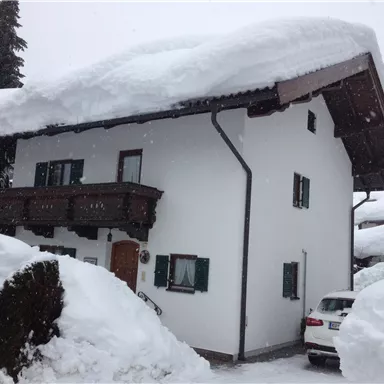 A house in the snow with a thick layer of snow on the roof. The surroundings are wintry and there is plenty of snow.