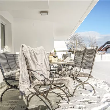 A winter balcony with white snow covers. Chairs with a blanket and a bright blue sky in the background.