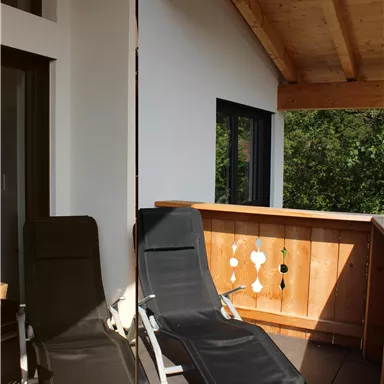 A relaxed balcony with two loungers and a wooden railing. The large front window provides plenty of daylight.
