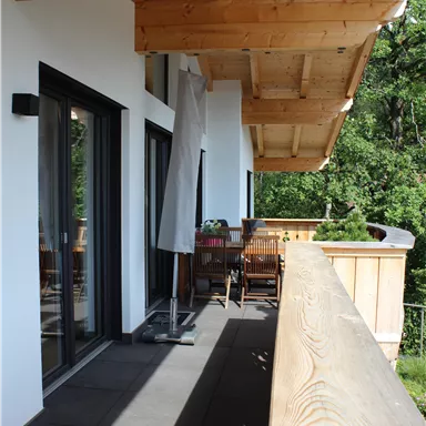 A modern balcony with a wooden railing and a view of greenery. There is a table with chairs and a sun umbrella.