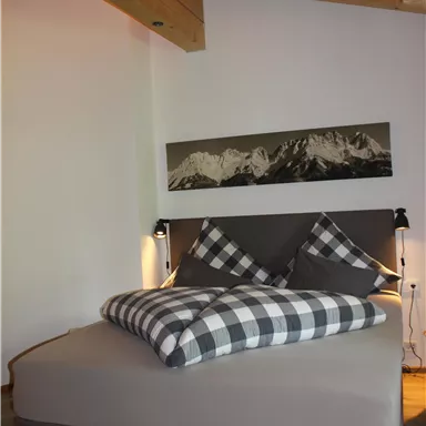 A modern bedroom with a comfortable bed and checkered pillows. The wooden ceilings and wall decorations create a cozy atmosphere.