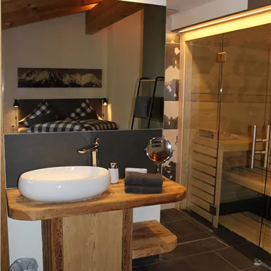 A modern bathroom with an elegant sink made of stone and wood. The shower has a glass door and there is a sauna in the background.