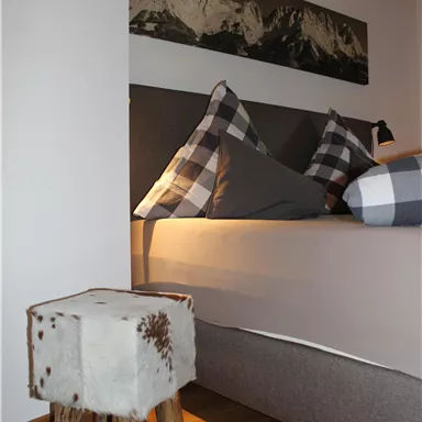 A cozy bedroom with a large bed and checkered pillows. Next to the bed is a small wooden stool.