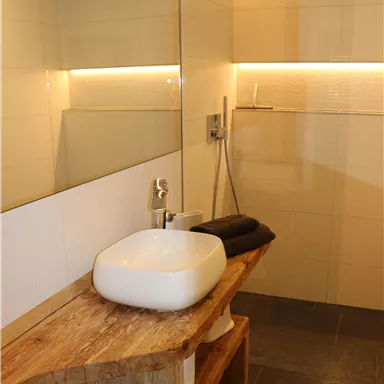 A modern bathroom with a wooden shelf and an elegant sink. The walls are light and well-lit, creating a cozy atmosphere.