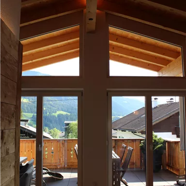 A modern room with large windows and a wooden ceiling. In the background, there is a beautiful view of the mountains and a balcony.