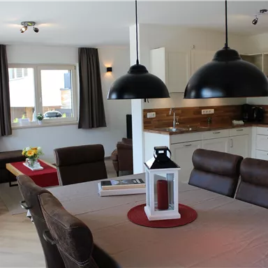 Ein modernes Wohnzimmer mit einer offenen Küche. Der Raum ist hell und einladend, mit einem Esstisch und gemütlichen Sitzgelegenheiten.