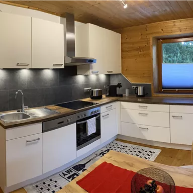 A modern kitchen with white cabinets and a wood decor. It is well equipped with appliances and a large window that lets in light.