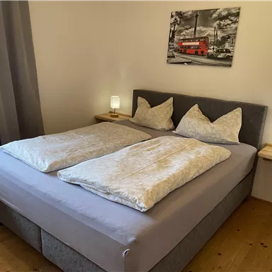 A comfortable bedroom with a large double bed and bright bedside tables. On the wall hangs a picture of a red bus.