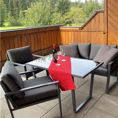 A cozy seating area on the terrace with a table and comfortable chairs. On the table, there is a bottle of wine and glasses, decorated with a red cloth.