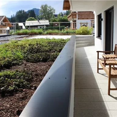 Ein schöner Balkon mit einer Holzbank und Blick auf eine grüne Landschaft. Im Hintergrund sind Häuser und Berge zu sehen.