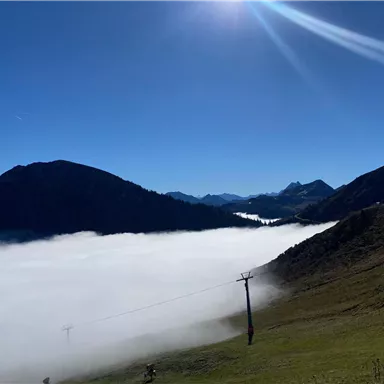 Eine malerische Berglandschaft mit tief hängenden Wolken im Tal. Der Himmel ist klar und sonnig, was die Schönheit der Natur unterstreicht.