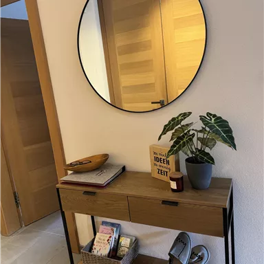 A modern entrance area with a round mirror and a stylish console table. Plants and some decorative items are placed on the table.