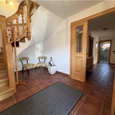 Ein einladender Flur mit einer Holztreppe und gemütlichem Mobiliar. Ein großer Teppich und fliesenboden verleihen dem Raum Wärme und Komfort.