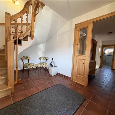 Ein einladender Flur mit einer Holztreppe und zwei Stühlen. Der Raum ist hell erleuchtet und hat braune Fliesen.