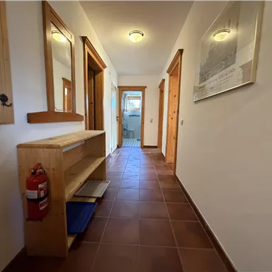 Ein heller Flur mit Holzverkleidungen und Spiegeln. Auf der linken Seite steht ein Schuhregal und an der Wand hängt ein Feuerlöscher.
