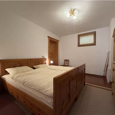 Ein gemütliches Schlafzimmer mit einem großen Holzbett und zwei Kissen. Die Wände sind hell, und es gibt einen Schrank sowie eine kleine Nachtkommode.