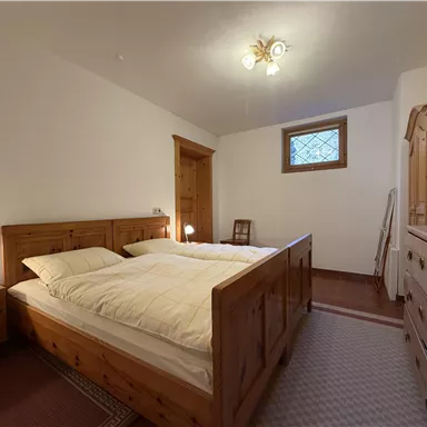 Ein gemütliches Schlafzimmer mit zwei Einzelbetten aus Holz. Die Wände sind hell und es gibt einen kleinen Fensterbereich mit natürlichem Licht.