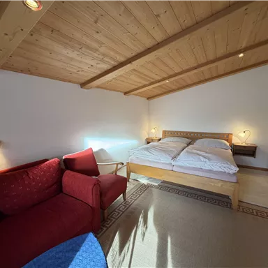 Ein gemütliches Schlafzimmer mit einem Doppelbett und einem roten Sofa. Das Holzdecken und die sanfte Beleuchtung sorgen für eine einladende Atmosphäre.