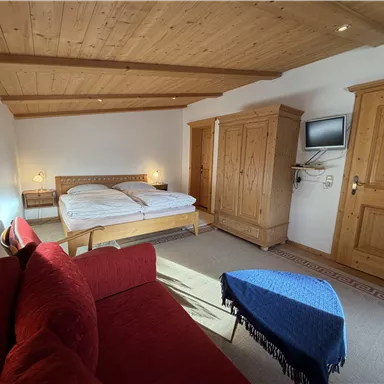 Ein gemütliches Schlafzimmer mit einem Doppelbett und einem roten Sofa. Der Raum hat Holzmöbel und einen Fernseher an der Wand.